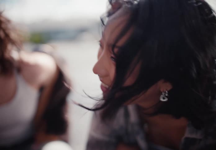 Candid slow-motion close-up of a joyful young Asian woman with braces and a nose ring laughing with friends, her hair blowing in the wind