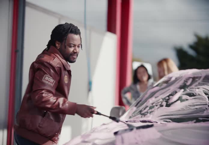 Slow motion shot of a man enthusiastically washing his car with pink foam at a self-service wash bay