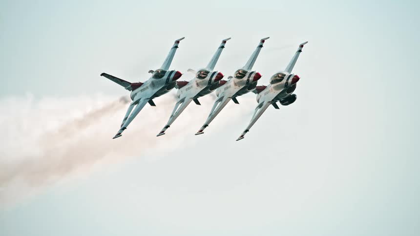 A squadron of four fighter jets fly in a synchronized diamond formation during a slow-motion aerial performance