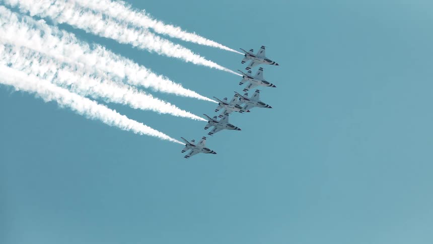 Stunning slow-motion footage of five fighter jets flying in tight formation with white smoke against a clear blue sky