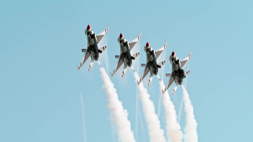 Four USAF Thunderbirds F-16 Fighting Falcons perform a slow-motion flyby, trailing white smoke across the sky
