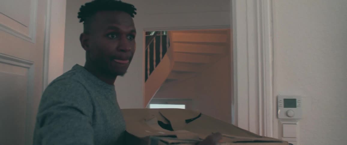 A young African American man carries a cardboard box as he moves into a new apartment
