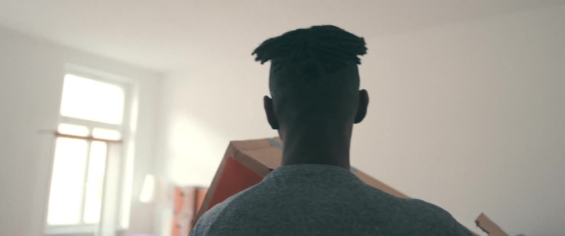 Slow motion shot from behind of a man carrying a large cardboard box into his new home
