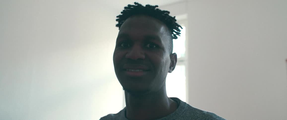 Close-up portrait of a young Black man with a gentle smile looking directly at the camera in a brightly lit room