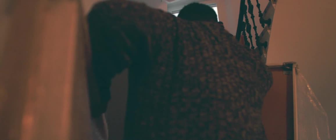 A mysterious low-angle shot from behind one person reveals another silhouetted figure at the top of a dimly lit staircase