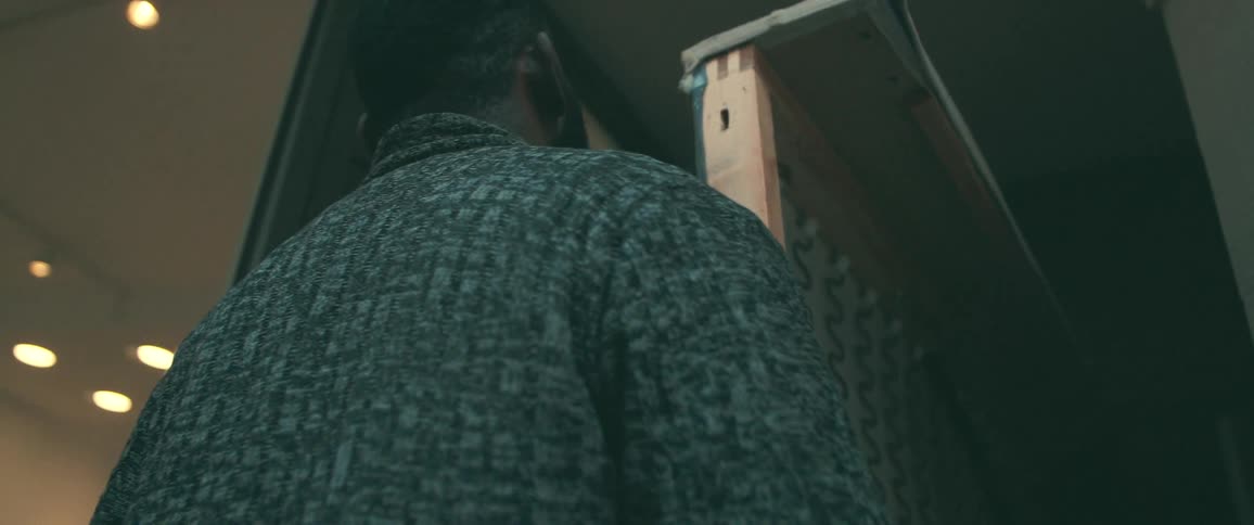 Over-the-shoulder view of a man in a textured sweater observing the wooden frame of a sofa in a workshop