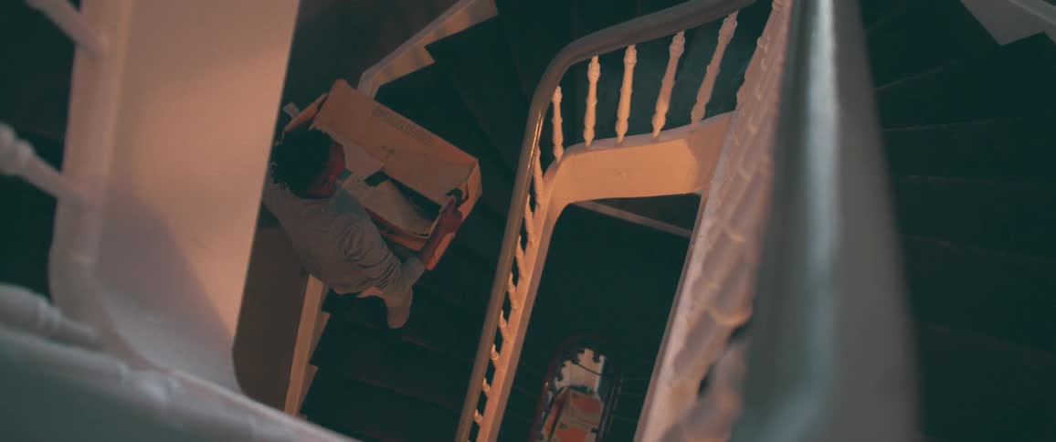 A person carefully carries a large box of belongings down a winding spiral staircase while moving