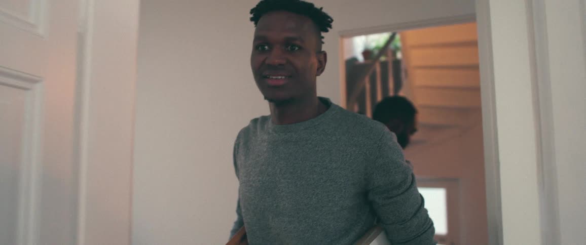 A happy young man smiles as he carries a picture frame while moving into a new home with his friend in slow motion