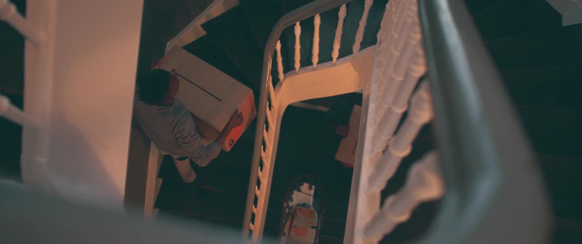High angle slow motion shot of two people carrying large moving boxes down a winding spiral staircase