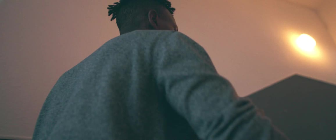 A young Black man seen from a low angle as he opens a large cardboard box inside his home