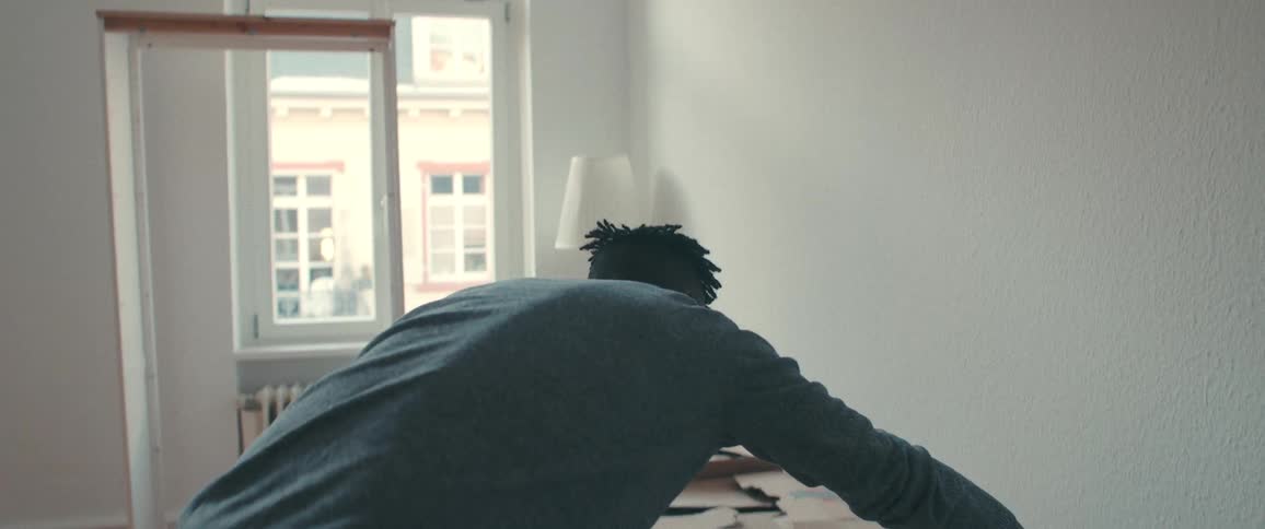 Slow pull-out shot from behind a man unpacking a large cardboard box while moving into his new, empty apartment