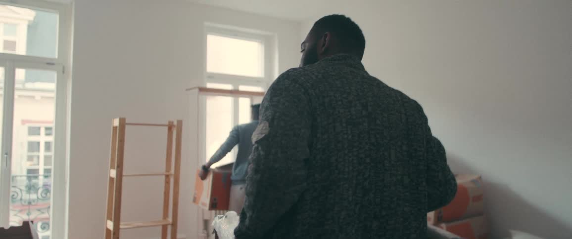 A slow motion back shot follows a man into his new apartment, where friends are busy moving in boxes