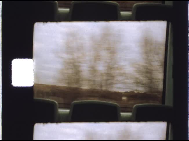 A nostalgic 8mm film scan shows a blurry countryside landscape passing by a train window on a cloudy day