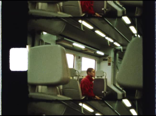 Vintage film scan shows a young man in a red sweatshirt sitting alone on a mostly empty train, looking out the window