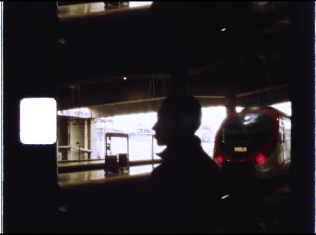 Vintage 8mm footage shows the silhouette of a person watching as a train pulls away from the station