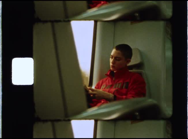 Candid film-style shot of a contemplative young person with a buzz cut riding on a train