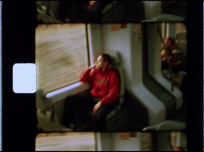 Vintage style film footage shows a thoughtful young person in a red sweatshirt looking out the window of a moving train