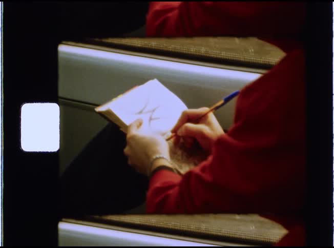 Super 8mm film captures a close-up of a person in a red sweater drawing in a sketchbook