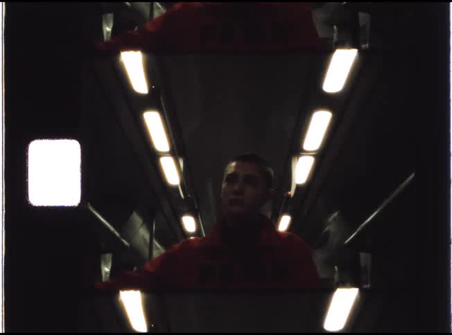 A moody, low-angle shot shows a pensive young person's reflection inside a dimly lit train car at night