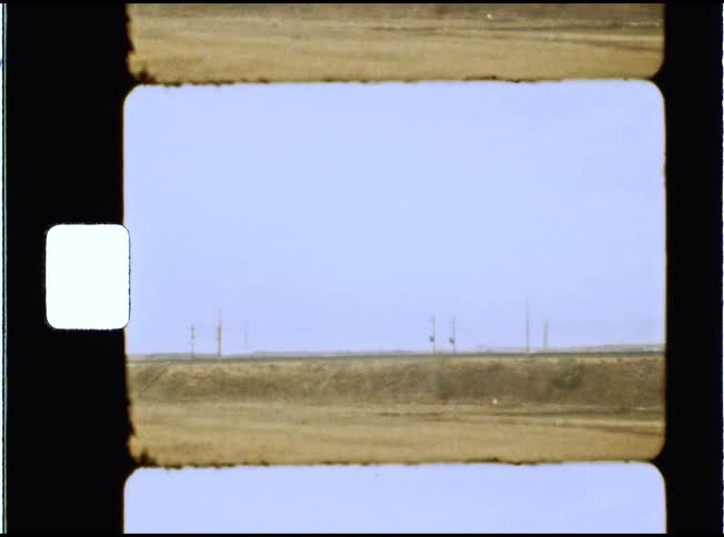 Vintage Super 8mm film strip shows a passing view of a desolate rural landscape with distant utility poles
