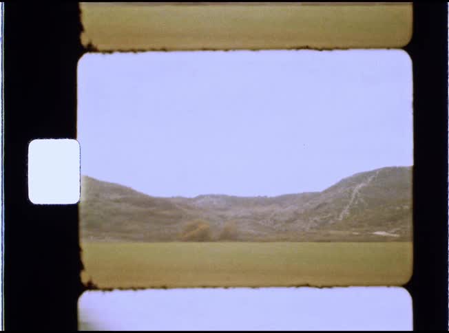 A young man sits by the window of a moving train, writing in a journal as the rural, hilly landscape passes by, captured on vintage film