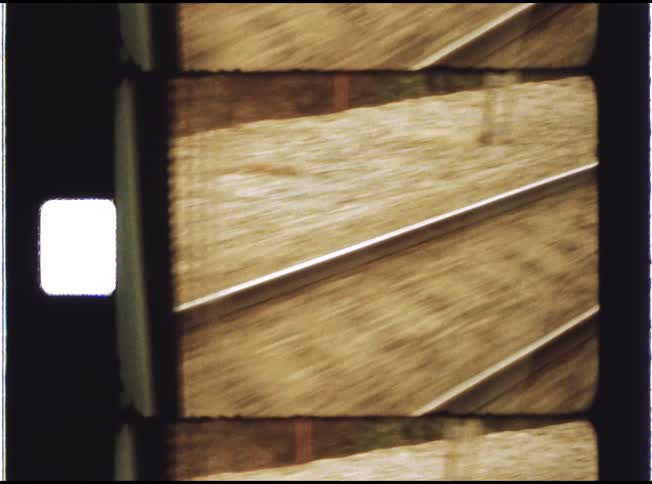 A point-of-view shot from a moving train shows railroad tracks rushing by, captured on vintage 8mm film with visible sprocket holes
