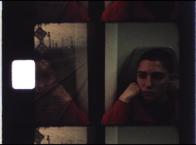 A contemplative young person with a buzz cut gazes out the window on a train, their reflection visible in the glass, all captured on a vintage film strip