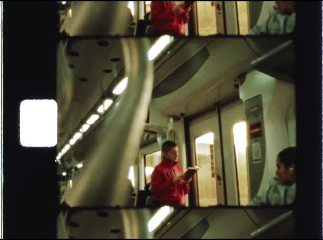A young man in a red sweatshirt reads a book while traveling on a modern train in this vintage 8mm film scan