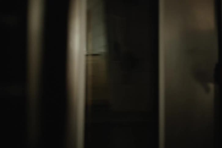 A shadowy figure is seen in a dark room before a hand slowly closes the door, creating a suspenseful and creepy atmosphere