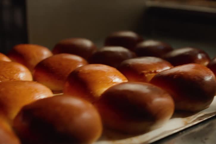 Close up of a tray of freshly baked golden brown brioche buns being placed on a metal counter to cool