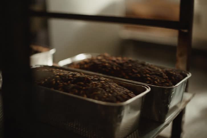 Freshly baked seeded loaves of bread cool in their tins on a metal rack in a bakery