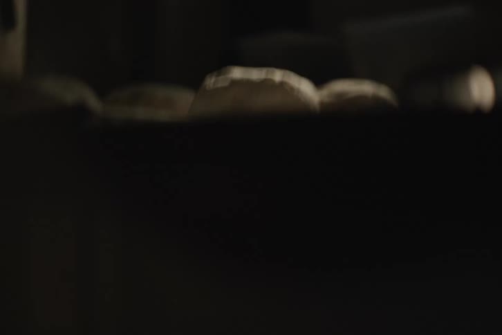 A cinematic tilt-down reveals fresh bread dough resting on a floured surface in a dimly lit, atmospheric bakery