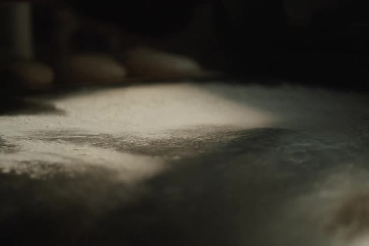 Dramatic slow motion shot of a baker dusting a metal table with flour before baking