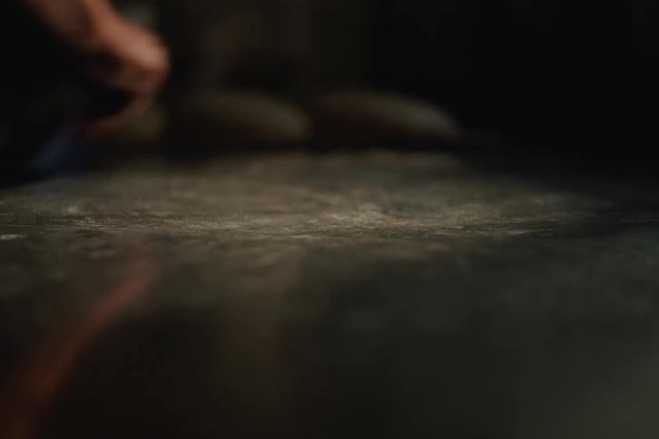 A person wipes down a dark, floured countertop with a blue scraper and their hand in preparation for baking