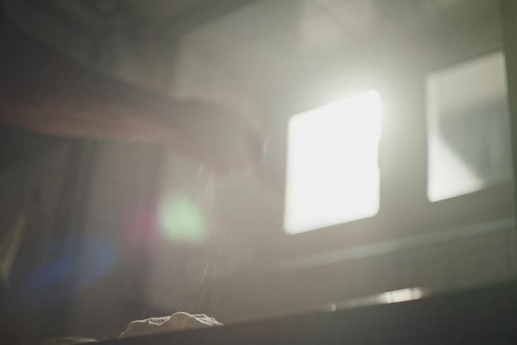 Cinematic slow motion shot of a baker's hands dusting fresh loaves of dough with flour in a sunlit kitchen
