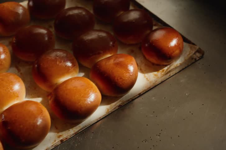 A tray of freshly baked glossy brioche buns is placed on a stainless steel kitchen counter