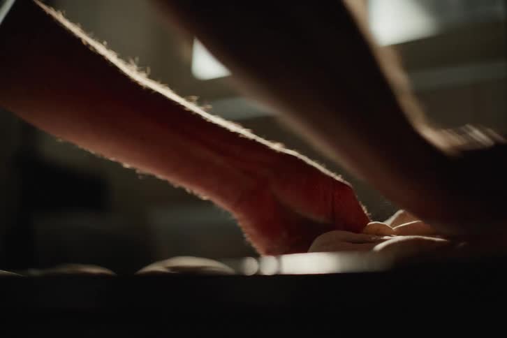 An artisan baker's hands skillfully knead bread dough in slow motion, backlit by morning sunlight