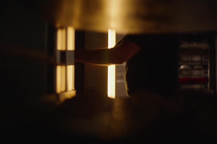 From inside the oven, a baker slides a large rack of raw dough into the hot industrial oven