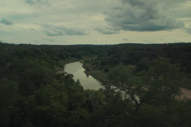 A scenic high-angle view of a tranquil river carving its way through a dense forest on a moody, overcast day