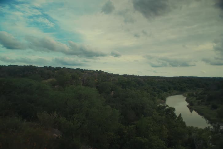 A wide, dramatic view of a river meandering through a dense, hilly forest under a cloudy sky