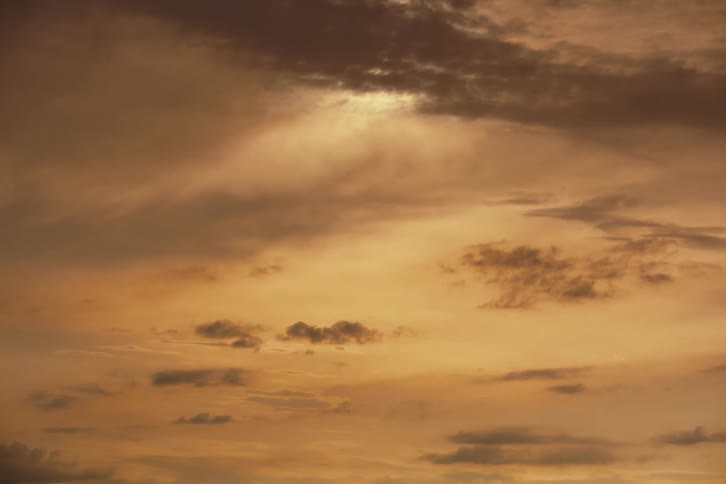 A serene and dramatic golden sky is filled with dark, moody clouds at sunset