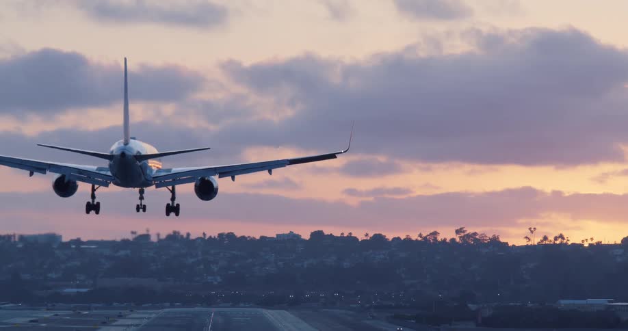 A passenger jet gracefully descends for a slow-motion landing on the runway against a beautiful purple and orange sunset sky