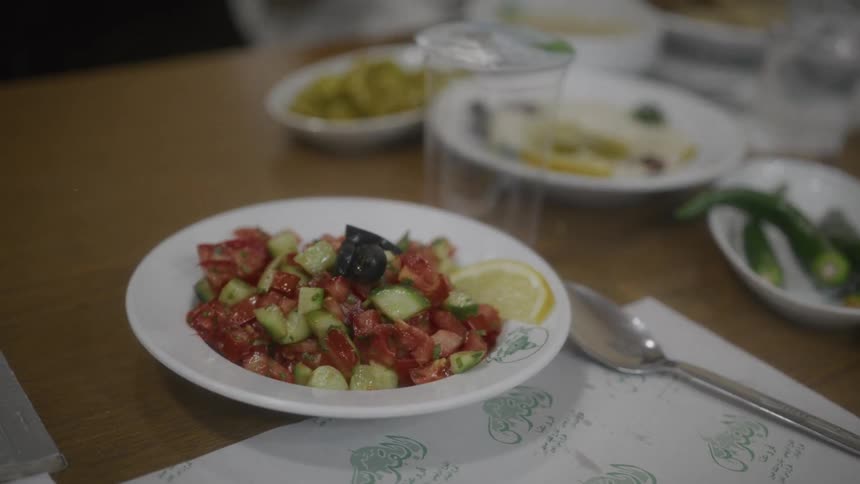 A fresh chopped tomato and cucumber salad sits in a white bowl on a restaurant table