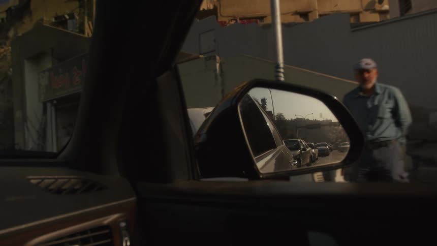 A view from inside a car focuses on the side-view mirror reflecting traffic on a city street