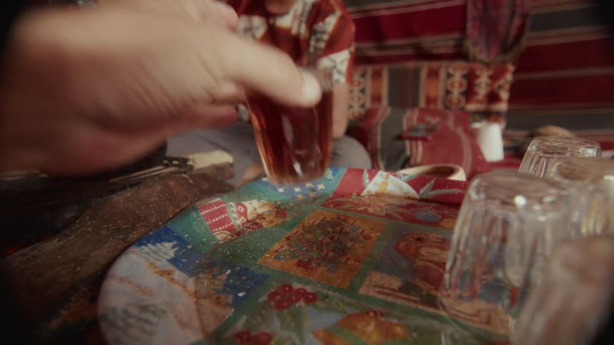 A hand picks up a traditional glass of tea in slow motion inside a cozy Bedouin tent