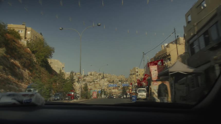 A first-person view from a car driving through the sunny streets of a historic city in Jordan