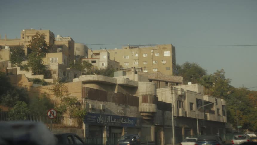 A point-of-view shot from a car driving through a city in Jordan, showing the sand-colored buildings on a hill