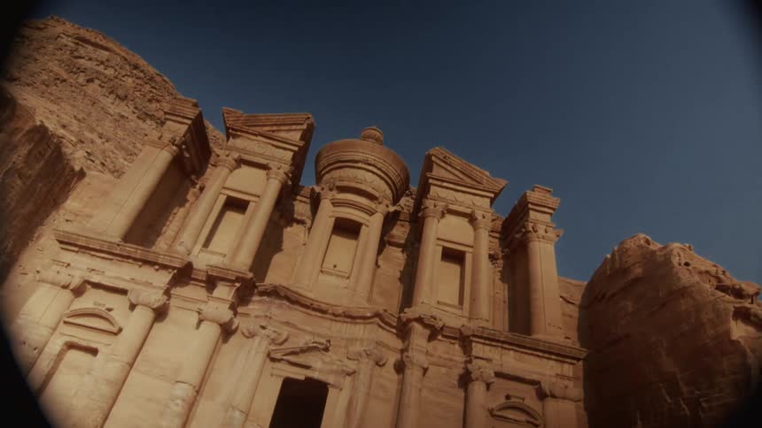 A vintage-style tilt-up shot reveals the magnificent ancient Monastery (Ad-Deir) carved into the rock in Petra, Jordan
