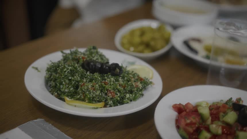 A close-up shot of a plate of fresh Tabbouleh salad alongside other Middle Eastern dishes on a wooden table