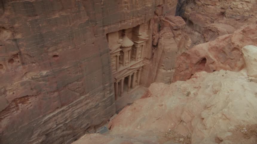 A high-angle slow pan reveals the magnificent Treasury building (Al-Khazneh) carved into the sandstone cliffs of Petra, Jordan